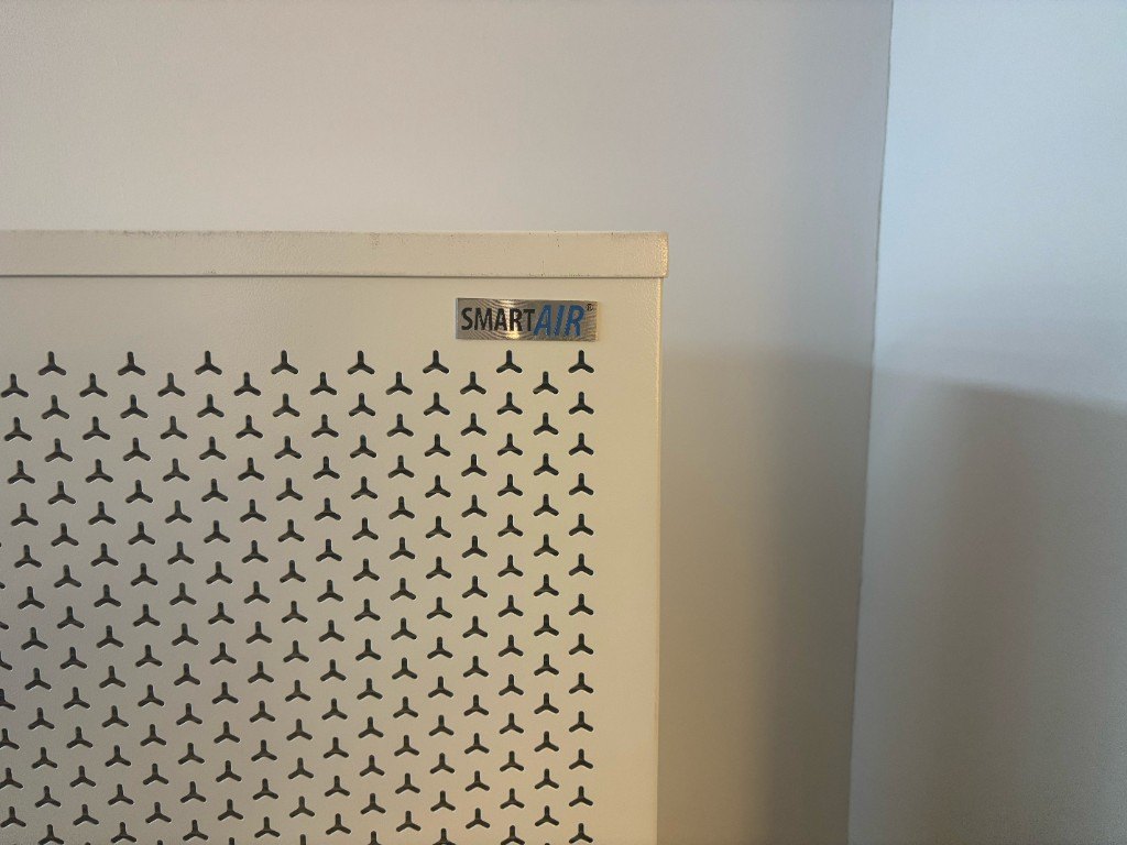 ภาพถ่ายมือถือระยะใกล้มุมบนของ Blast: โลหะพ่นสีขาว เจาะรูรูปตัว Y และป้าย Smart Air