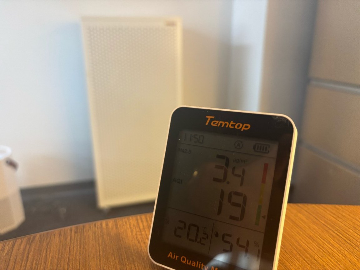 เครื่องวัดคุณภาพอากาศ Temtop S1 บนโต๊ะไม้ แสดงค่า PM2.5 3.4 µg/m³ มี Smart Air Blast ตั้งชิดผนังอยู่ด้านหลัง